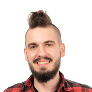 Man with mohawk hairstyle, beard, and red plaid shirt smiling at camera against white background