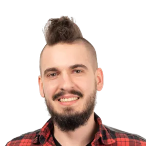 Man with mohawk hairstyle, beard, and red plaid shirt smiling at camera against white background