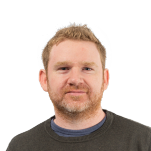 Headshot of a man with light brown hair and facial hair wearing a dark colored shirt against a white background.