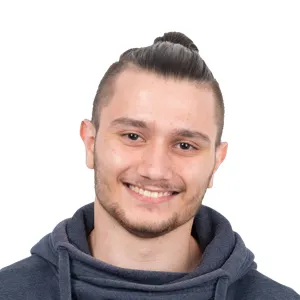Headshot of a smiling young man with dark hair styled in a top knot, wearing a dark navy hoodie against a white background.