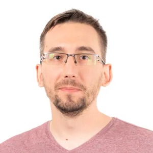 Headshot of a man wearing clear-framed glasses and a mauve v-neck shirt against a white background.