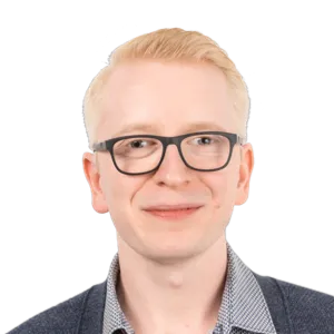 Headshot of a young man with blonde hair and glasses wearing a checkered shirt and dark sweater against a white background.