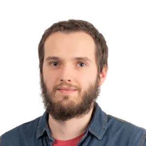Headshot of a bearded man with short brown hair wearing a denim shirt over a red shirt against a white background.