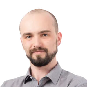 Headshot of a man with a beard wearing a gray button-up shirt against a white background.