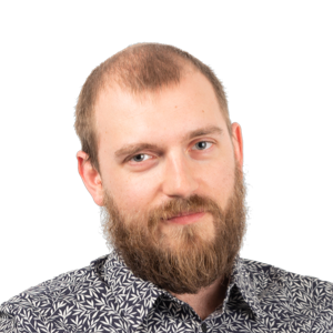 Headshot of a bearded man with short light brown hair wearing a patterned gray and black shirt against a white background.