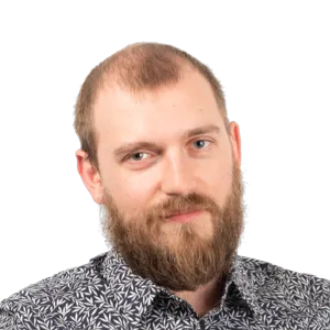Headshot of a bearded man with short light brown hair wearing a patterned gray and black shirt against a white background.