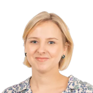 Blonde woman with short hair wearing a patterned top and dark earrings, smiling at camera against white background