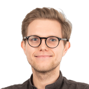 Headshot of a smiling man with blonde hair, glasses, and dark clothing against a white background.