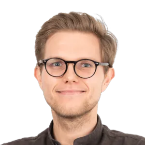 Headshot of a smiling man with blonde hair, glasses, and dark clothing against a white background.