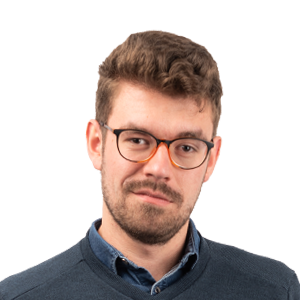 Headshot of a man with brown hair, beard, and glasses wearing a dark blue shirt against a white background.