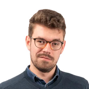 Headshot of a man with brown hair, beard, and glasses wearing a dark blue shirt against a white background.