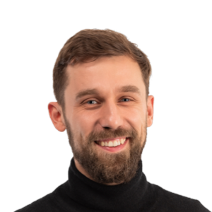 Headshot of a smiling man with brown hair and beard wearing a black turtleneck against a white background.