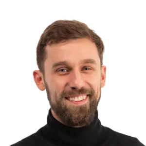 Headshot of a smiling man with brown hair and beard wearing a black turtleneck against a white background.