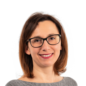 Professional headshot of a smiling woman with shoulder-length brown hair and glasses, wearing a gray top against a white background.