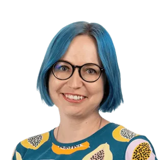 Portrait of a smiling person with blue hair and glasses wearing a teal and yellow patterned shirt against a white background.