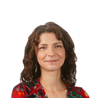 Portrait photo of a woman with shoulder-length curly brown hair wearing a red and green patterned top against a white background.