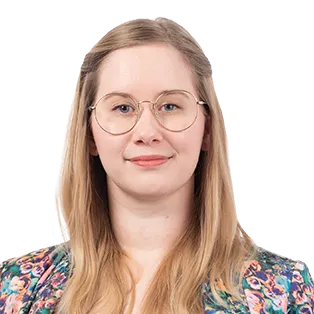 Portrait of a woman with long blonde hair and glasses wearing a colorful floral patterned shirt against a white background.
