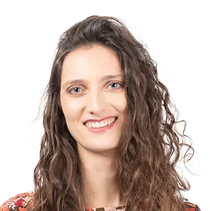 Professional headshot of a smiling woman with long, wavy dark hair wearing a colorful patterned top against a white background.