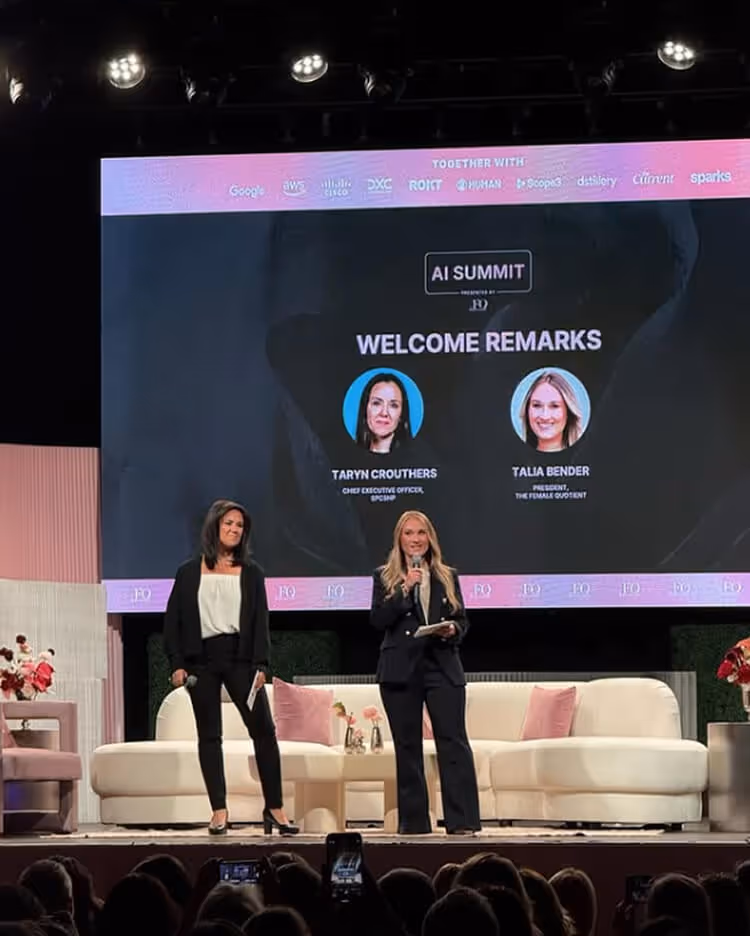 Two women standing on stage during AI Summit welcome remarks, with their photos and titles displayed on a large screen behind them.