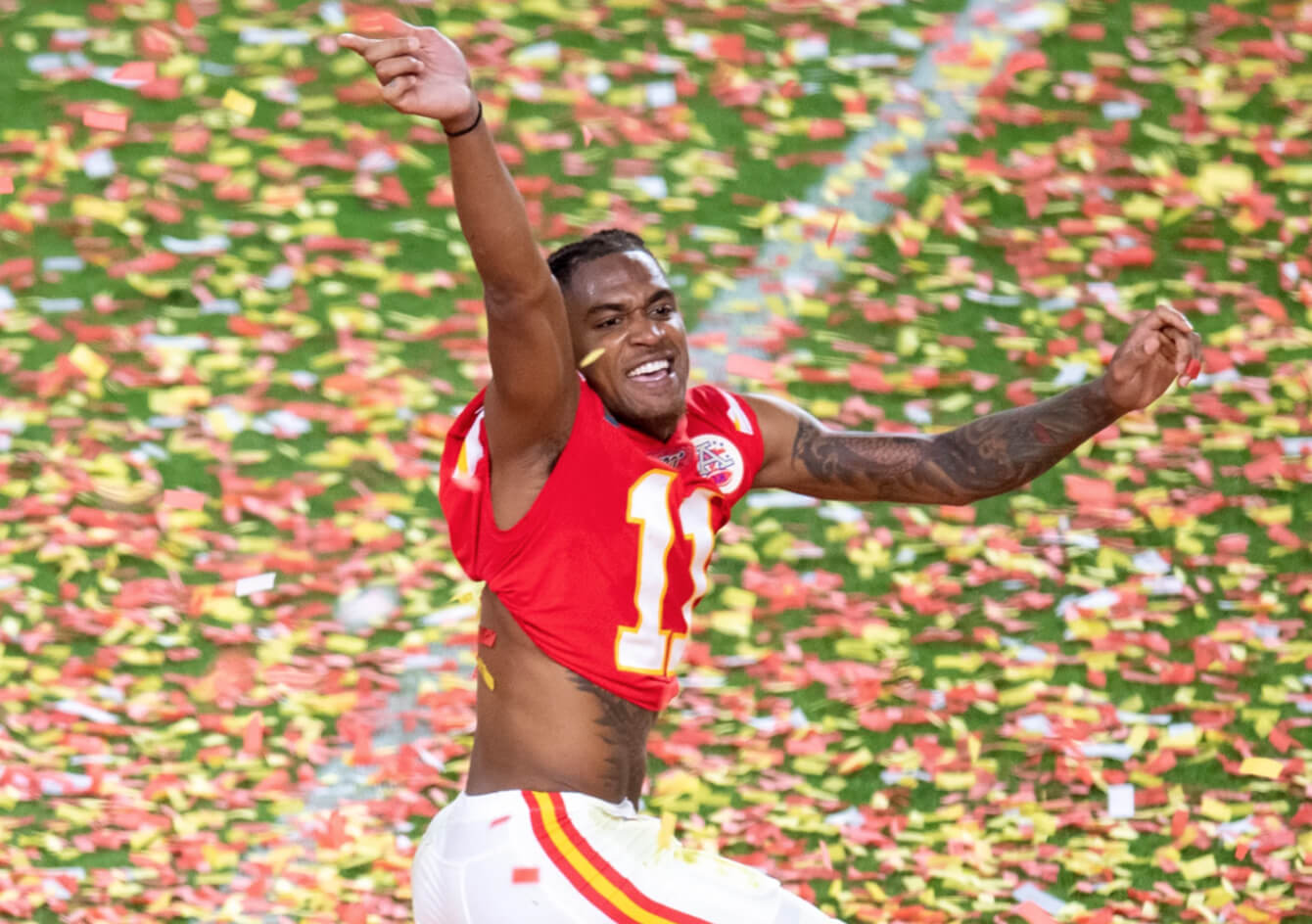 Kansas City Chiefs football player celebrating with arms raised amid red and yellow confetti on the field.