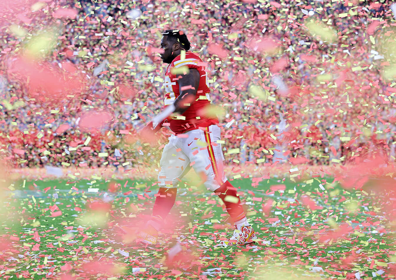Kansas City Chiefs player walking on a football field surrounded by red and yellow confetti.