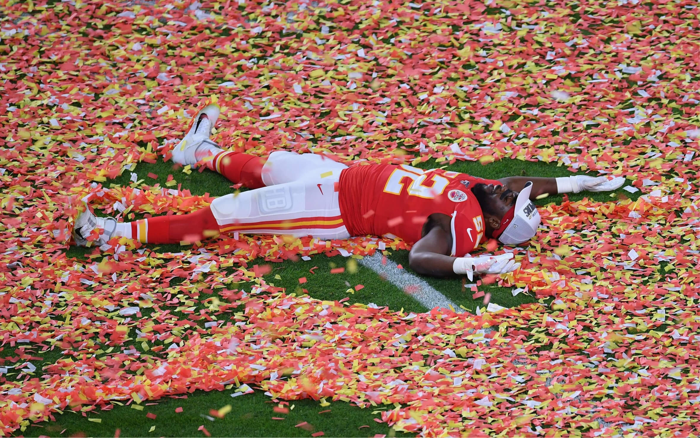 NFL player in a red Kansas City Chiefs uniform lying on the field covered in red, yellow, and white confetti.