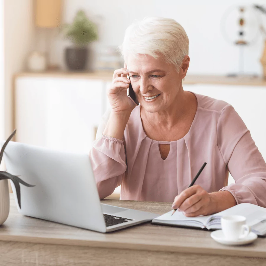 Senior woman on the phone, gaining clarity and planning with her laptop and notebook to secure a comfortable retirement.
