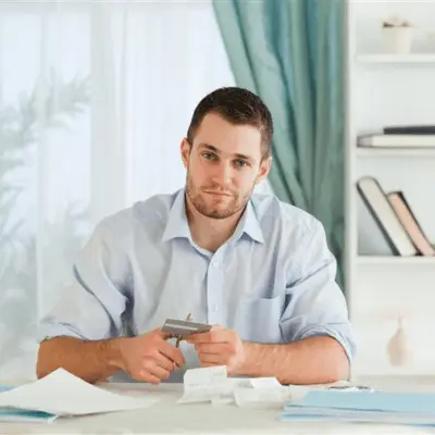 A man seated at a table with cutting a credit card and papers, after participating in a credit counseling session.