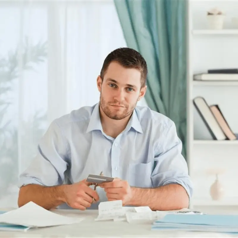 A man seated at a table with cutting a credit card and papers, after participating in a credit counseling session.