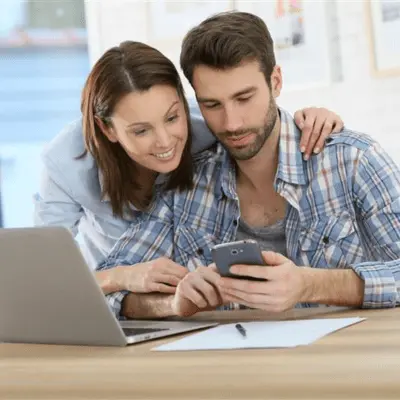 Happy couple reviewing information on phone and laptop, getting guidance through trusted housing counseling services.