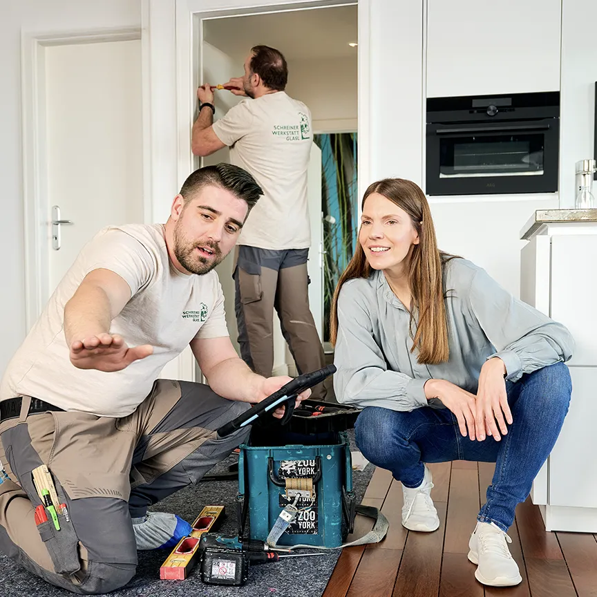 Ein Schreinergeselle bespricht die Arbeitsschritte des Bodenverlegens mit einer Kundin.