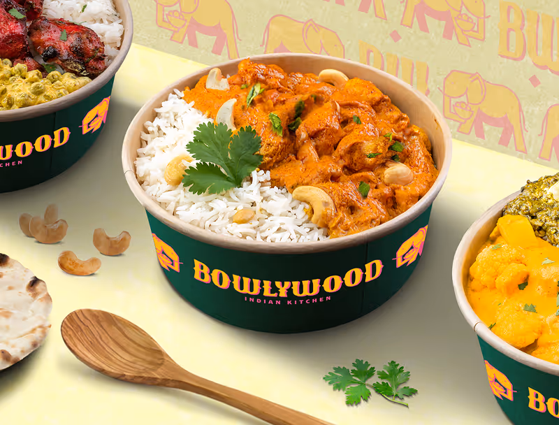 Bol vert de cuisine indienne contenant du riz blanc, du poulet au curry orange garni de noix de cajou et coriandre, entouré de noix de cajou, d'une cuillère en bois, pain naan et deux autres bols de nourriture.