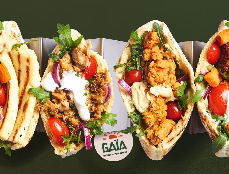 Quatre pitas garni de poulet grillé, poulet frit, légumes frais comme tomates cerises et oignons rouges, et sauces diverses, sur un support métallique avec un fond vert foncé.