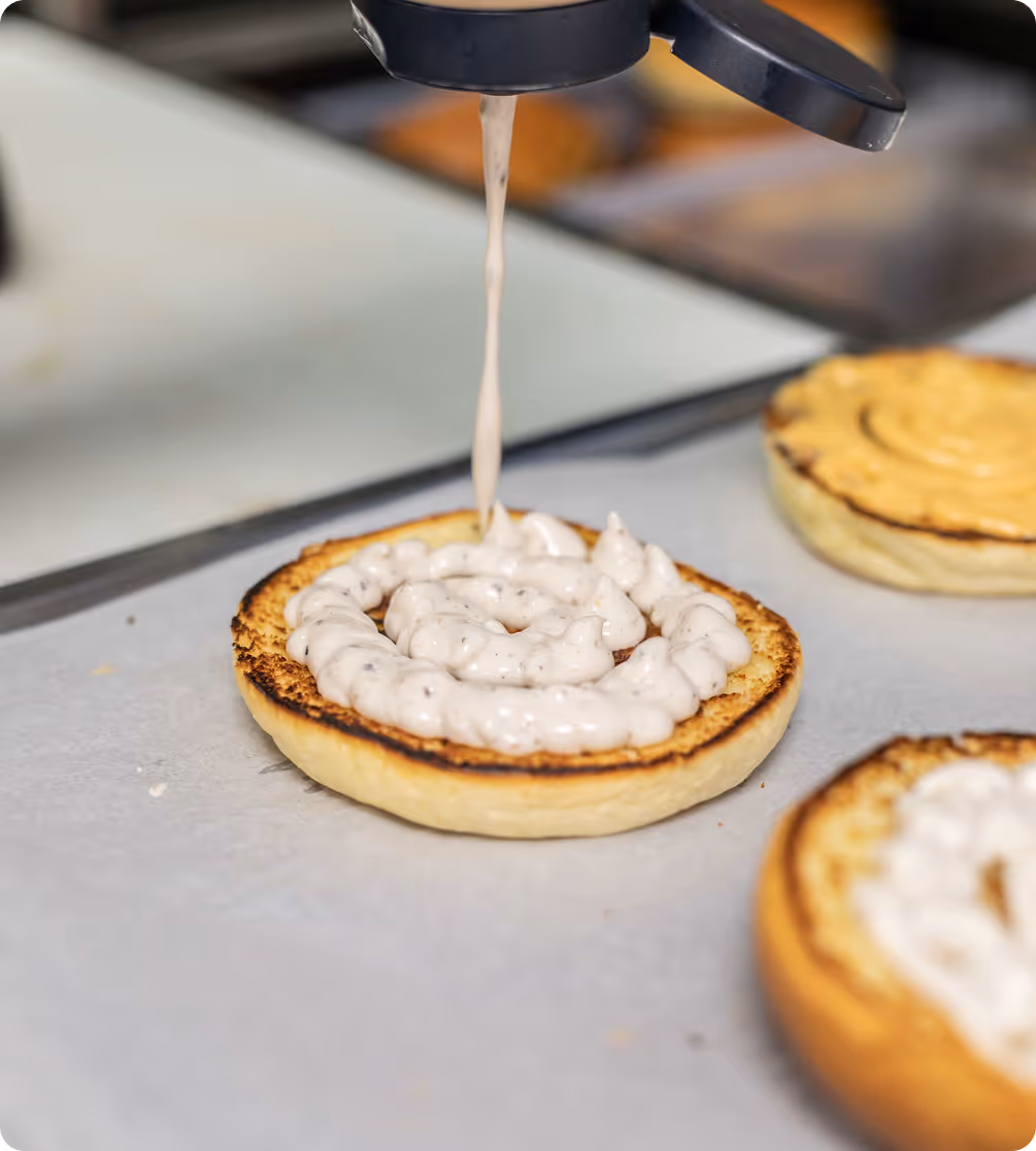 Un pain grillé en train d'être garnis de sauce blanche en spirale à partir d'un distributeur.