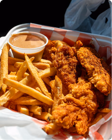 Portion de poulet frit croustillant avec frites dorées et une petite coupelle de sauce crémeuse.