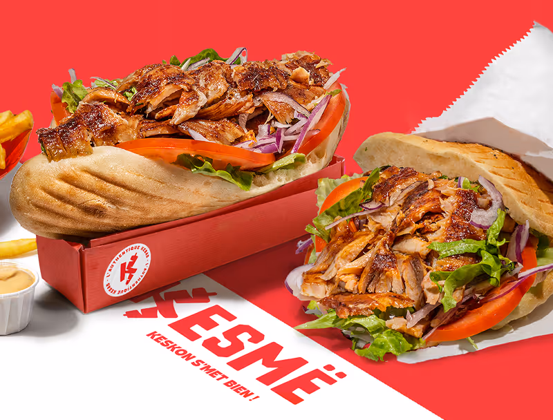 Deux sandwiches au poulet grillé avec salade, tomates et oignons rouges, servis avec des frites et une sauce à l'ail.