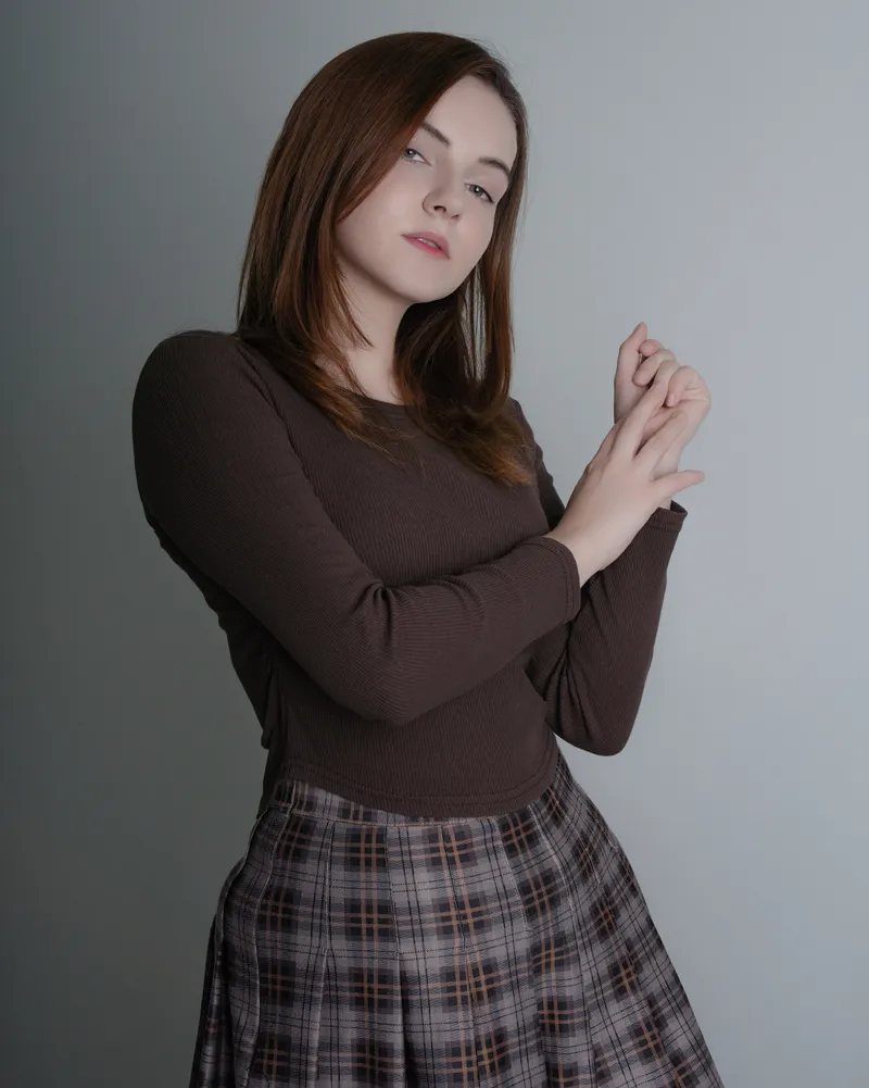 Studio portrait of a woman wearing a brown top and plaid skirt.