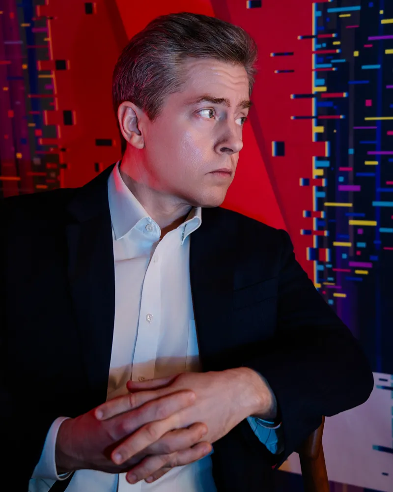 Studio portrait of a man in a suit against a red and blue cyberpunk backdrop.