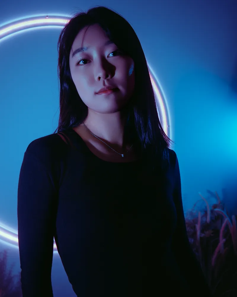 Studio portrait of a woman under blue lighting beside a curved neon light.