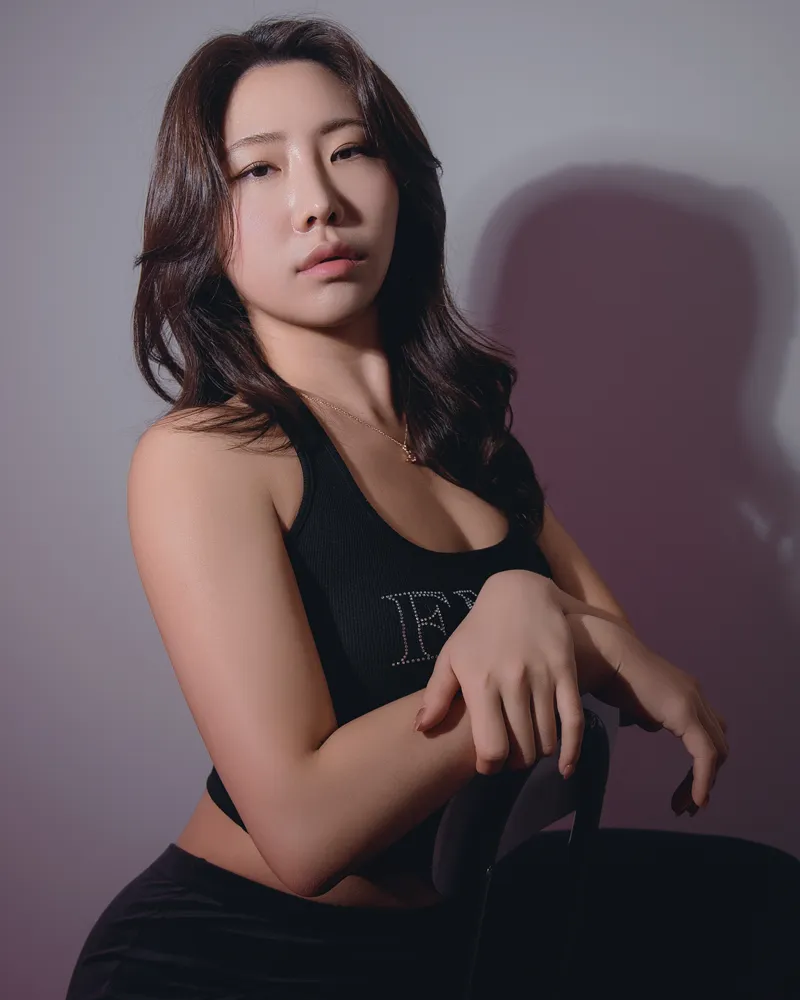 Seated studio portrait of a woman in a black top against a grey background.