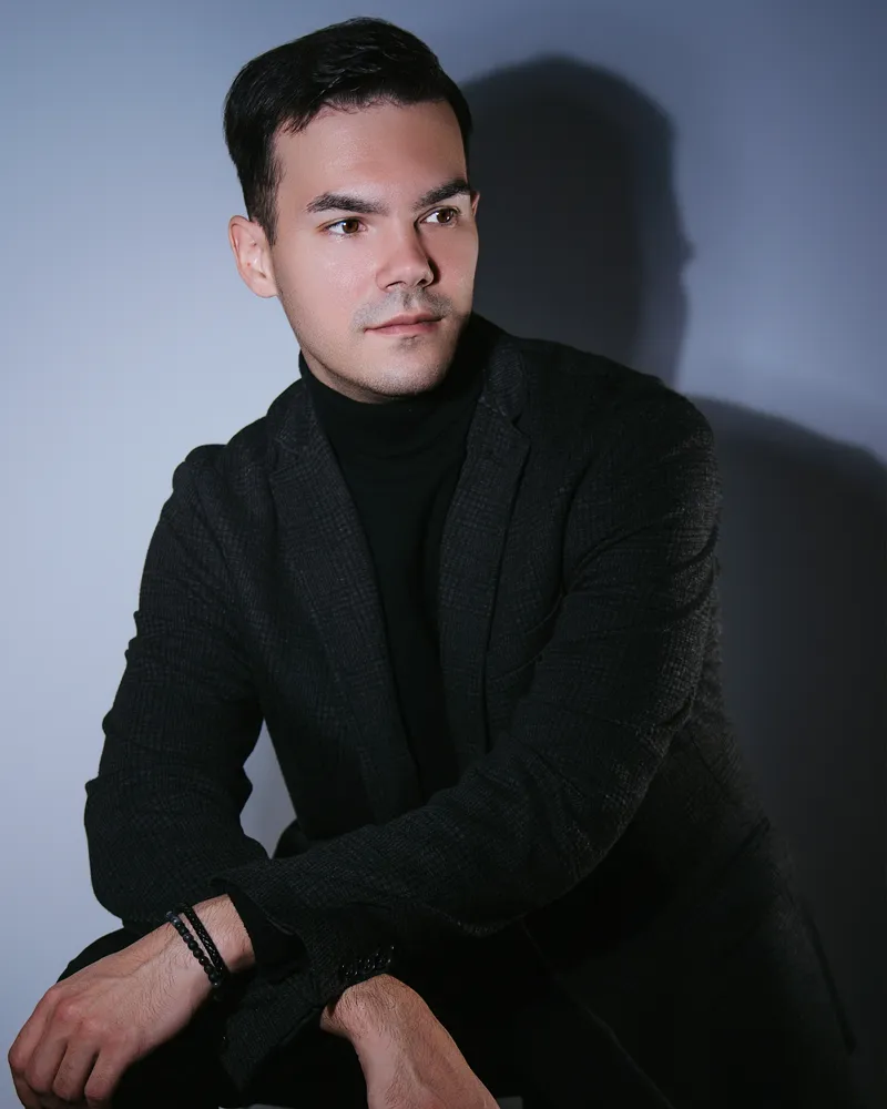 Seated studio portrait of a man in a black jacket and turtleneck.