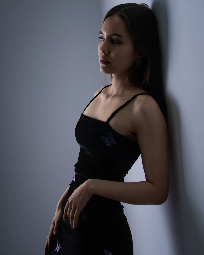 Studio portrait of a woman leaning against a wall in a black dress.