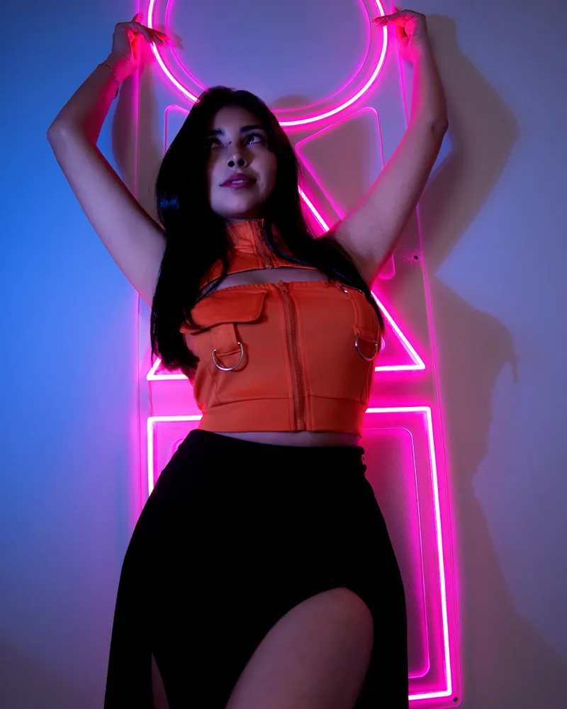 A woman posing with raised arms in front of pink geometric neon lights.