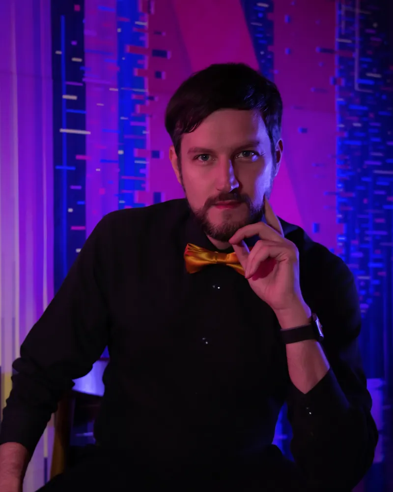 Studio portrait of a man wearing a bow tie under purple and blue lighting.