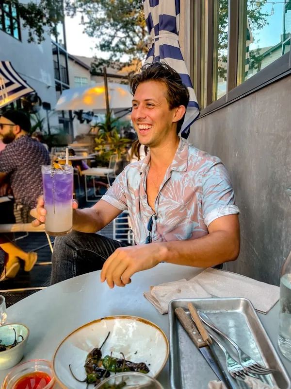 A smiling man enjoying a cocktail at a restaurant bar.