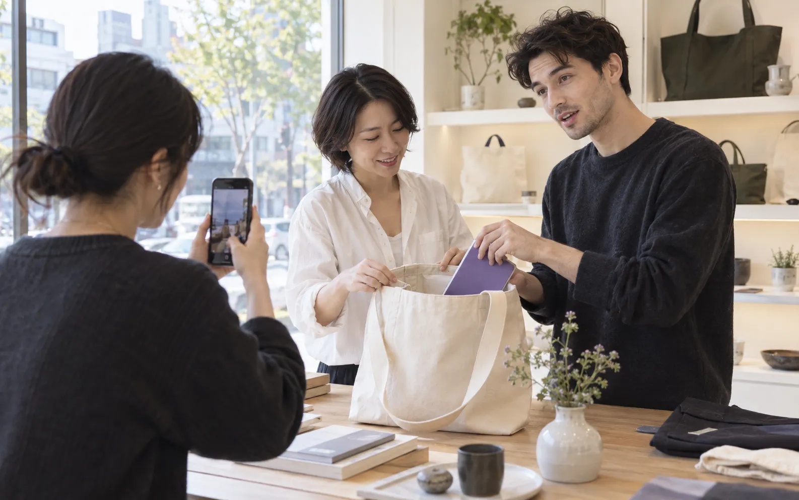 A shop owner and creator demonstrating a bag while a collaborator films.