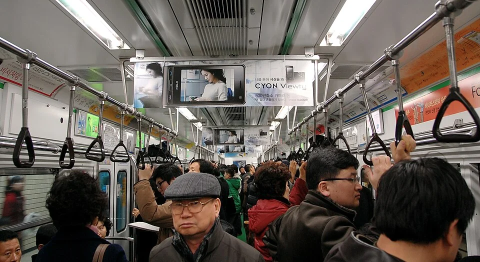 Passengers sitting and standing inside a crowded Seoul subway carriage.