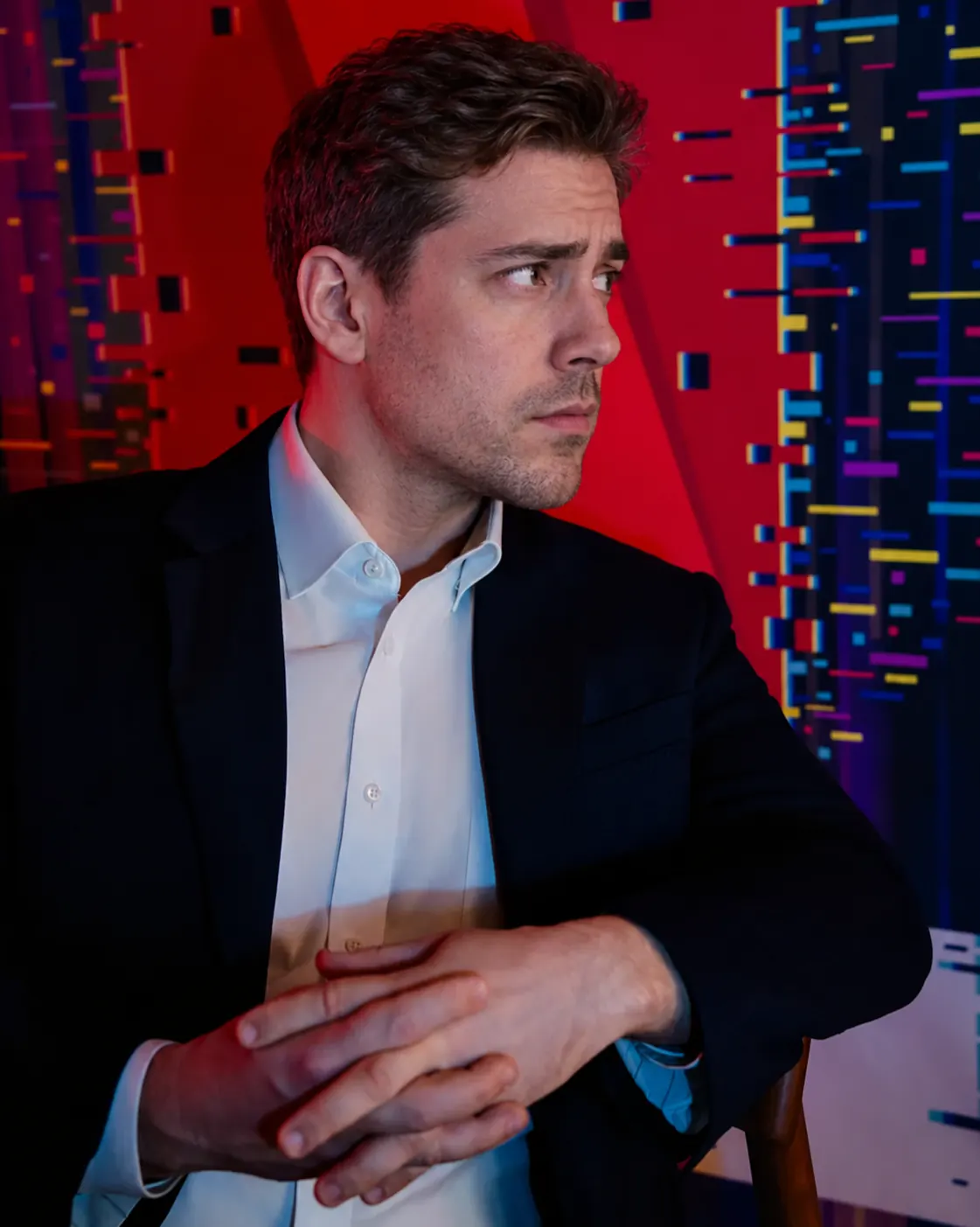 Original PIN Studio concept portrait of a man in a suit against a red and blue backdrop. His face has been replaced with an AI-generated identity.