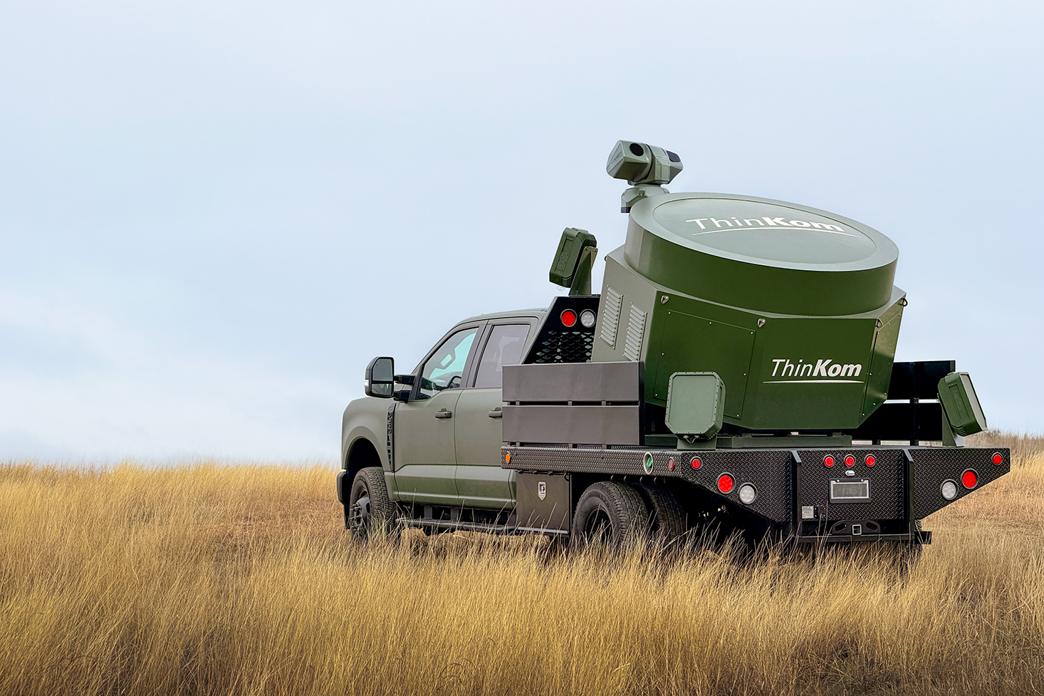ThinKom Alecto high-power microwave effector integrated onto a mobile truck platform, stationed in a grassy field.