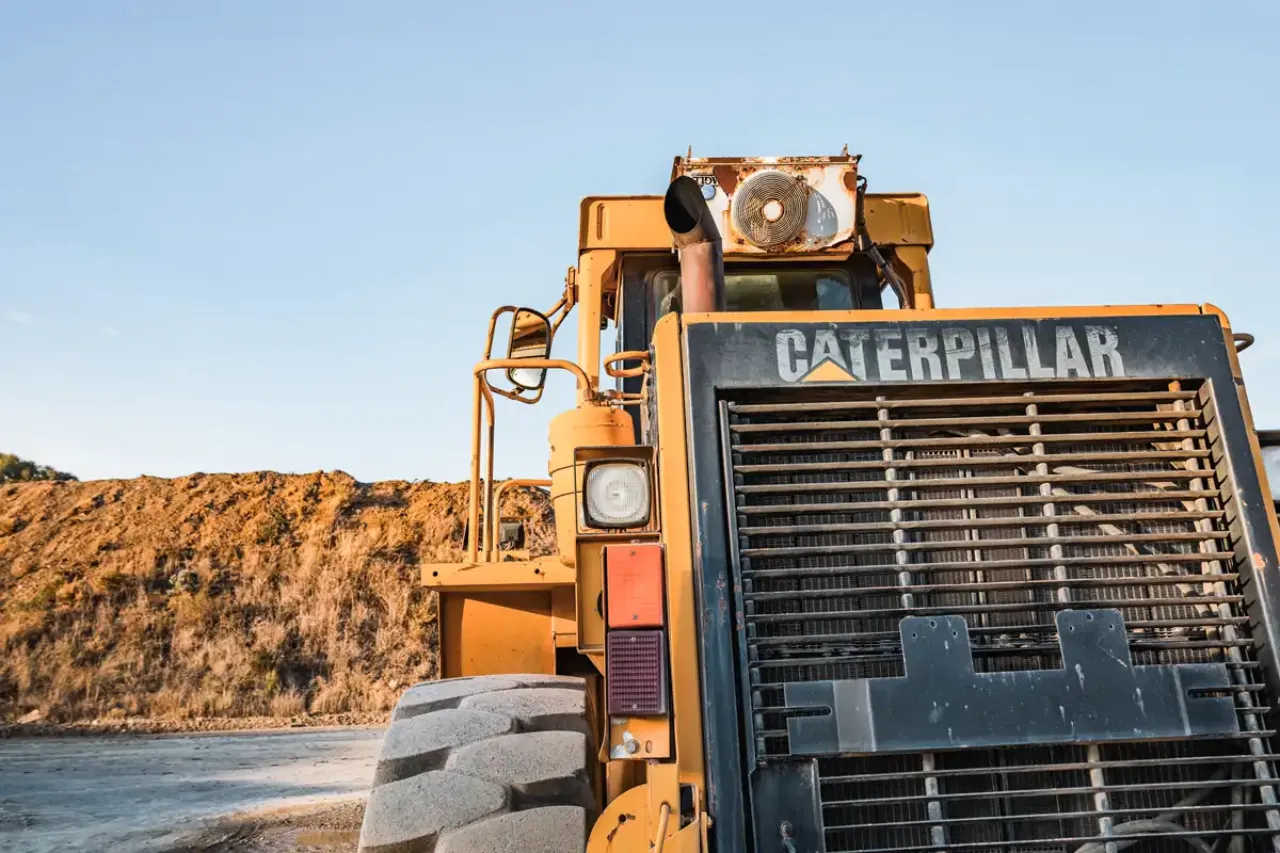 Front view of yellow Caterpillar heavy equipment at construction site, large tires and metal grille visible against clear blue sky.